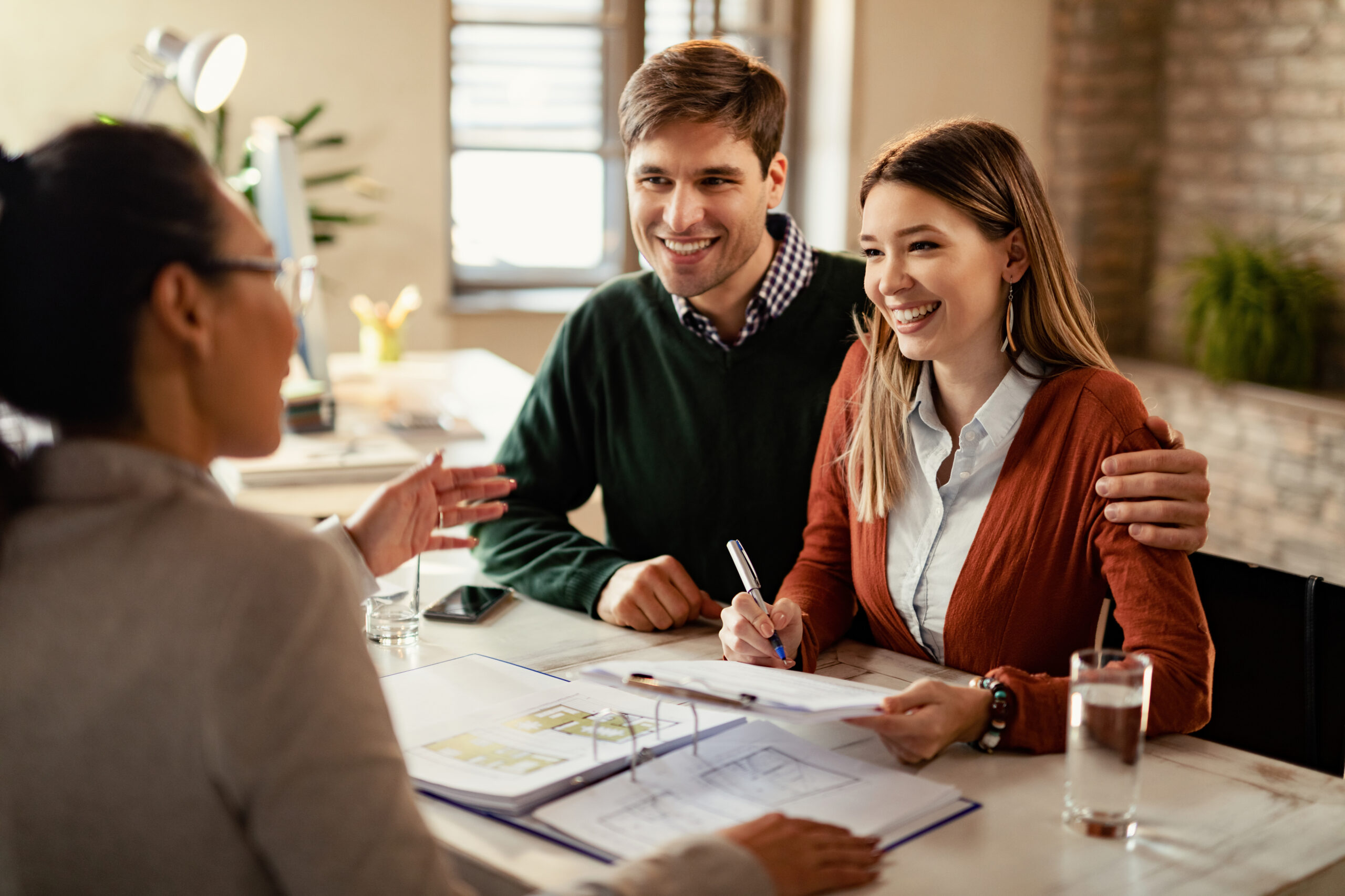 Young happy couple signing a contract while being on a meeting with insurance agent in the office.